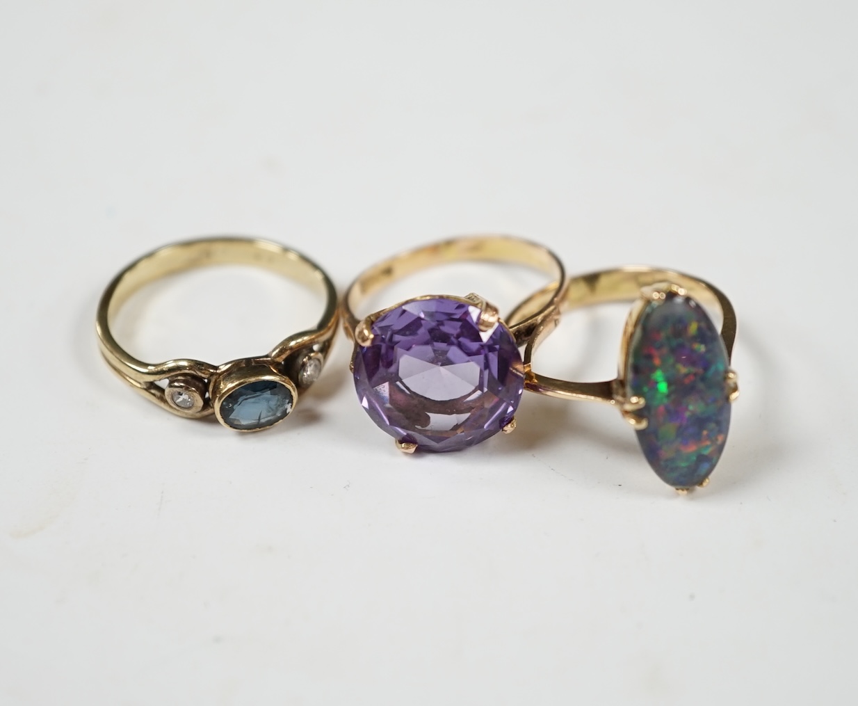 A 14k and black opal double set oval ring, size N, a yellow metal, sapphire and diamond set three stone ring and a Middle Eastern yellow metal and synthetic colour change corundum set ring, gross weight 8.9 grams. Condit